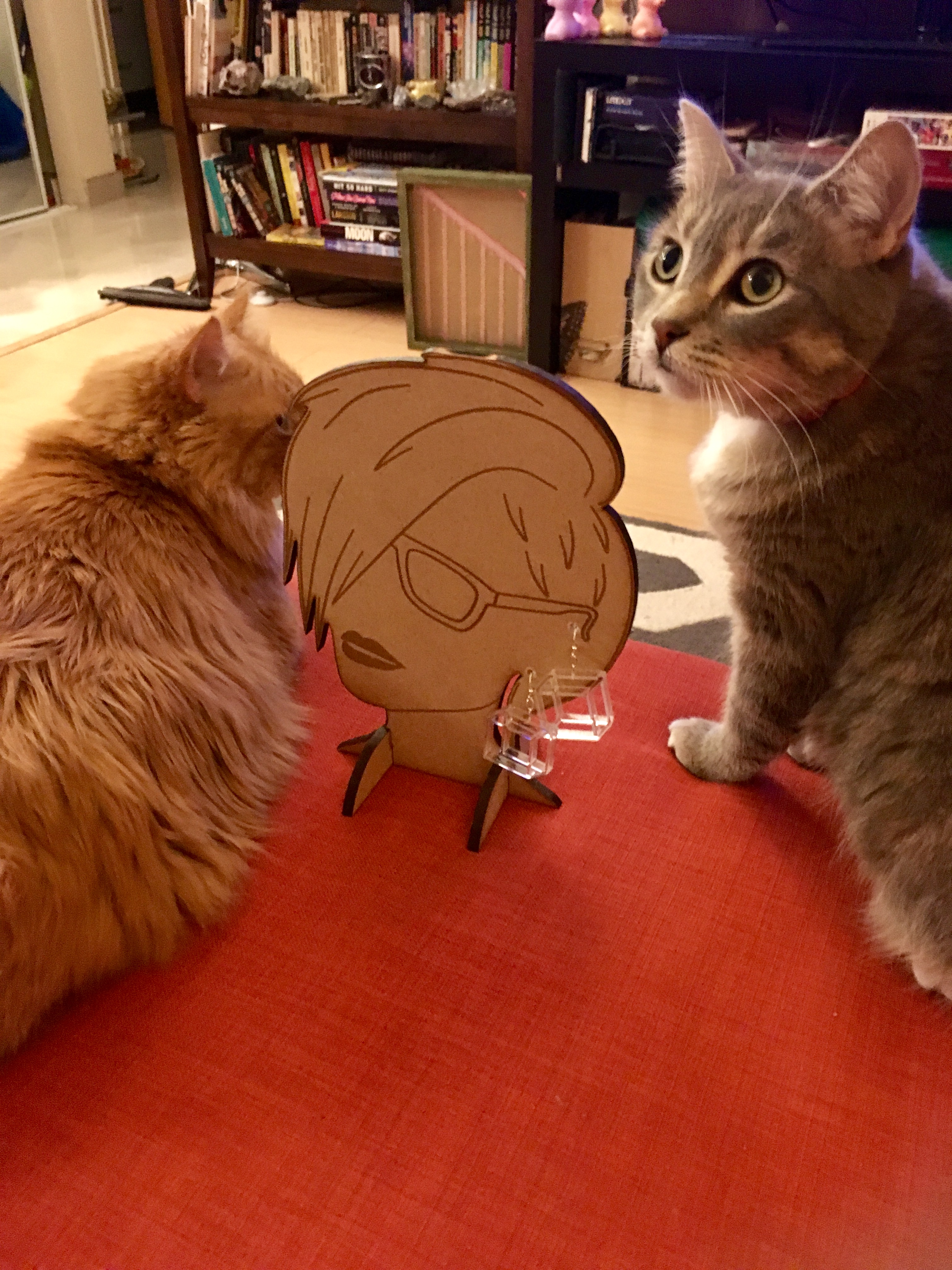 Two cats investigating earrings on a laser cut and engraved display stand shaped like a woman's head